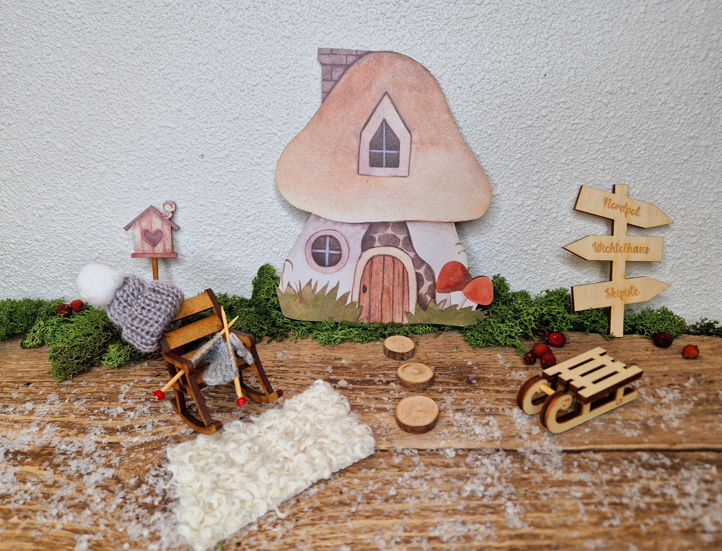 Schaukelstuhl aus Holz mit Mütze und Strickzeug als Miniatur vor Wichtelhaus