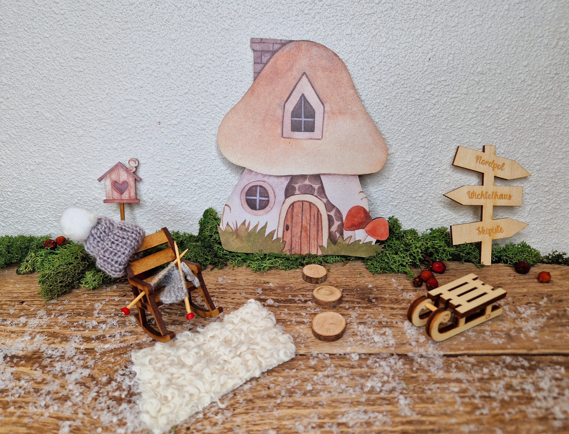 Schaukelstuhl aus Holz mit Mütze und Strickzeug als Miniatur vor Wichtelhaus
